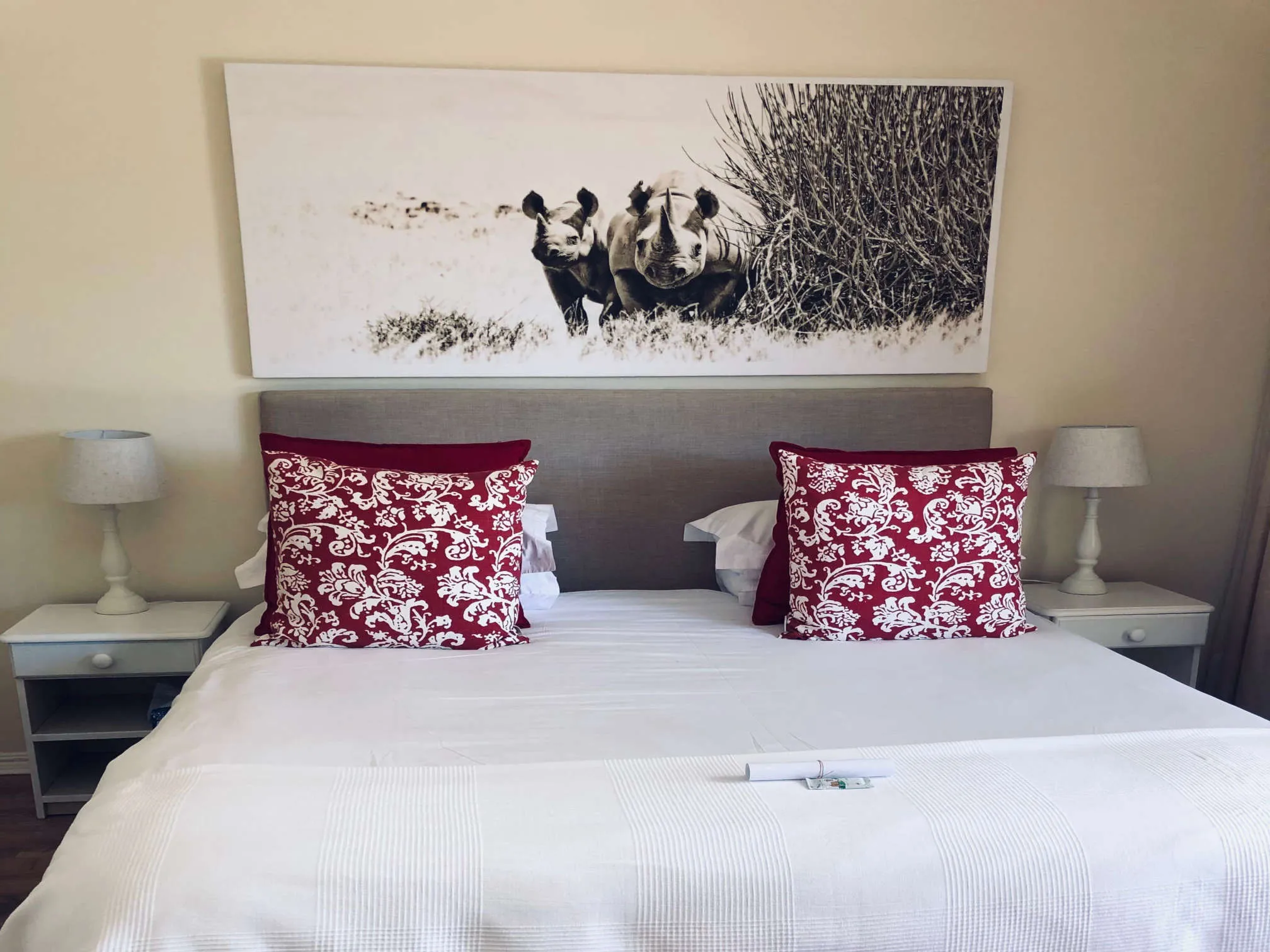 Bed with red and white pillows flanked by lamps with a rhino artwork above