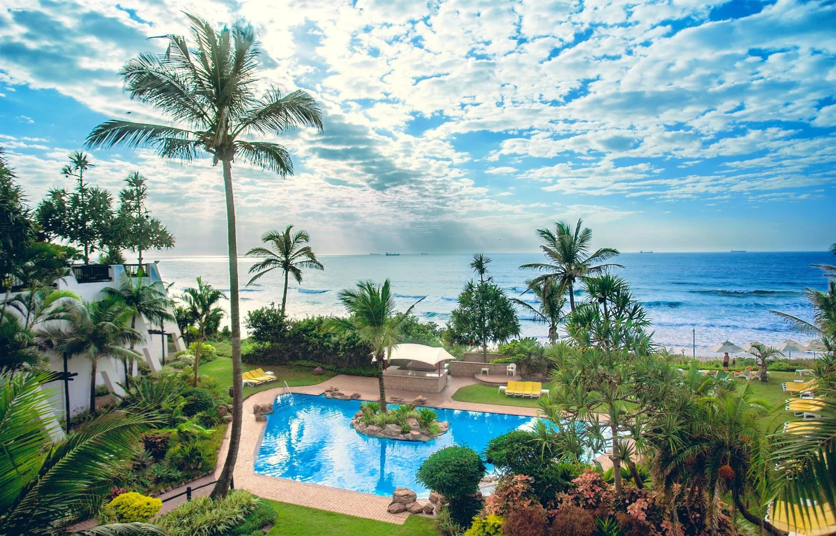 Tropical resort with pool palm trees and ocean view under a partly cloudy sky