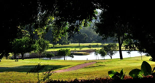 Golf course with water hazard trees and pathway under sunny sky