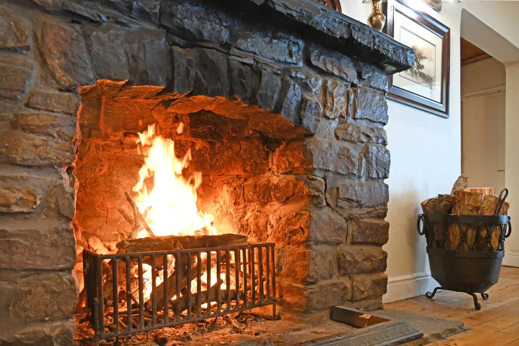 Stone fireplace with a blazing fire and a basket of firewood beside it