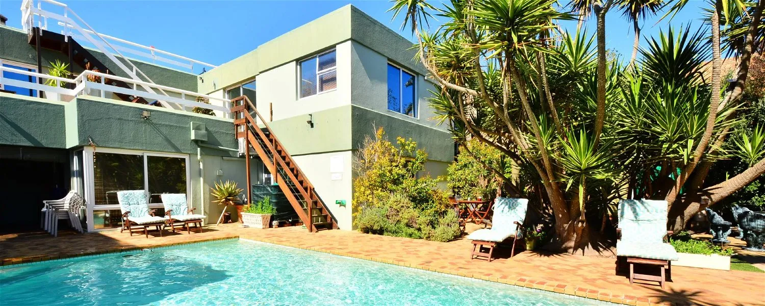 Modern house with pool lounge chairs and lush greenery in a sunny setting