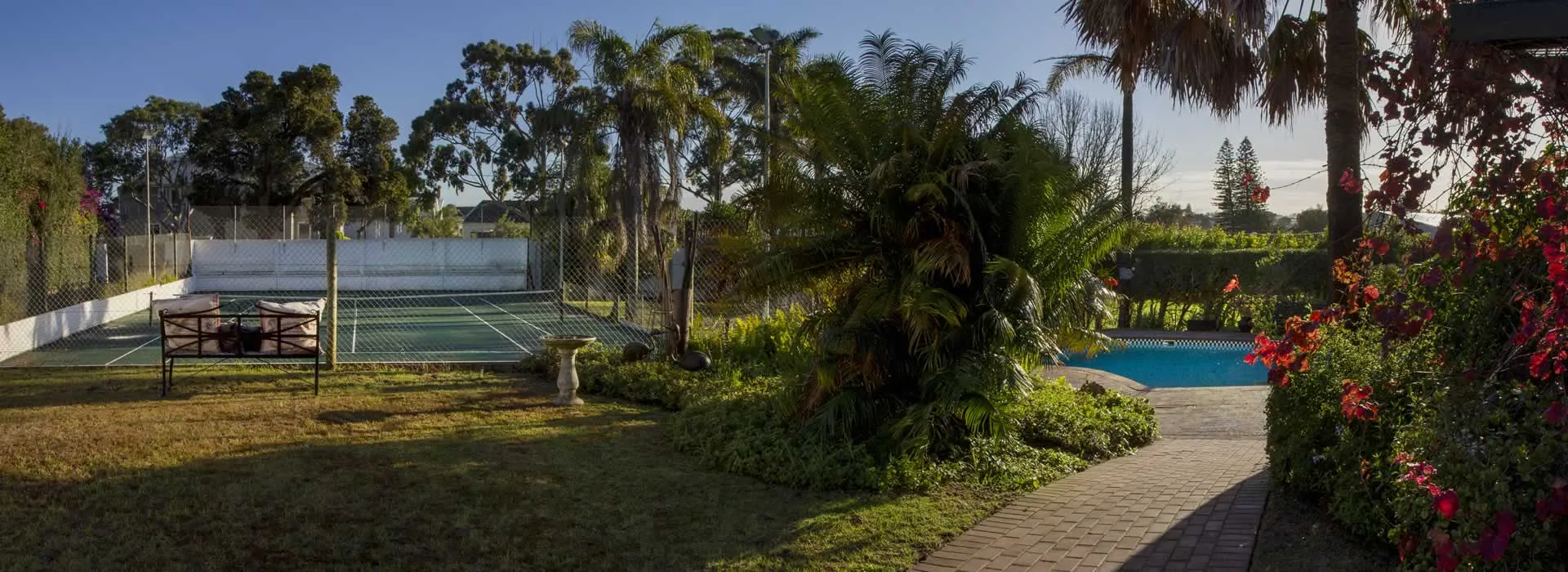 Tennis court and swimming pool surrounded by lush greenery and flowers