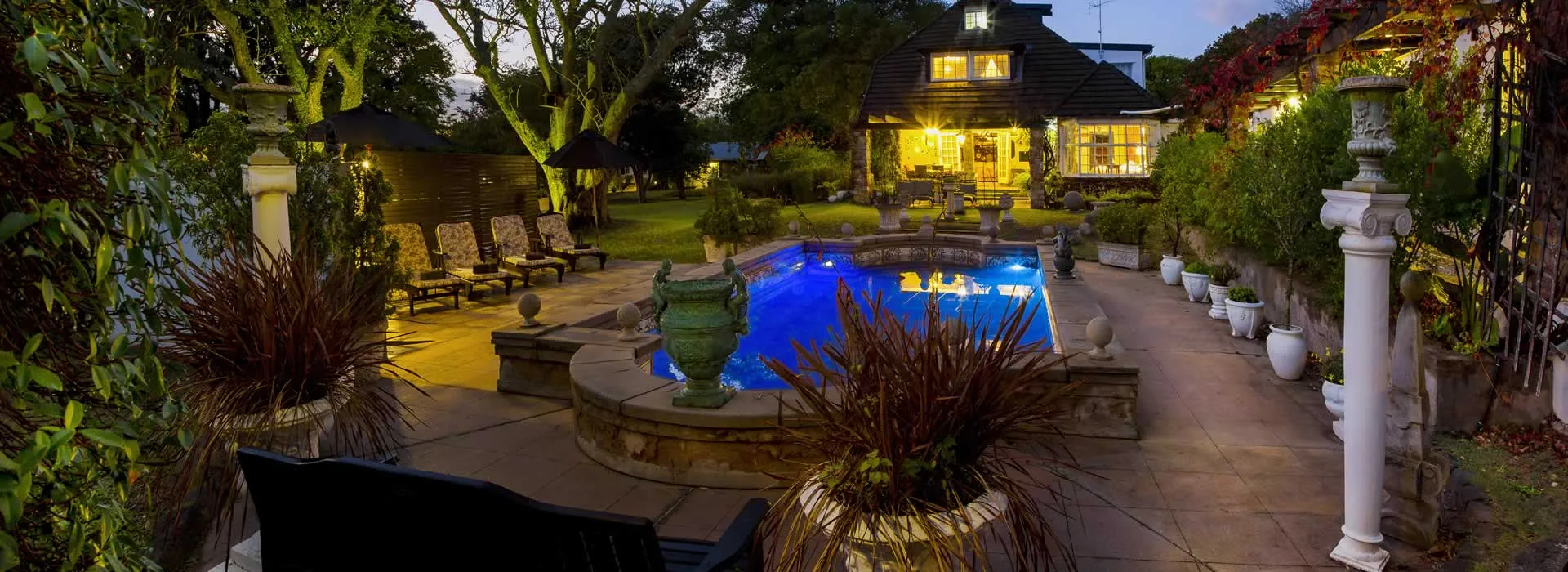 Evening view of a lit pool garden and house with outdoor seating area
