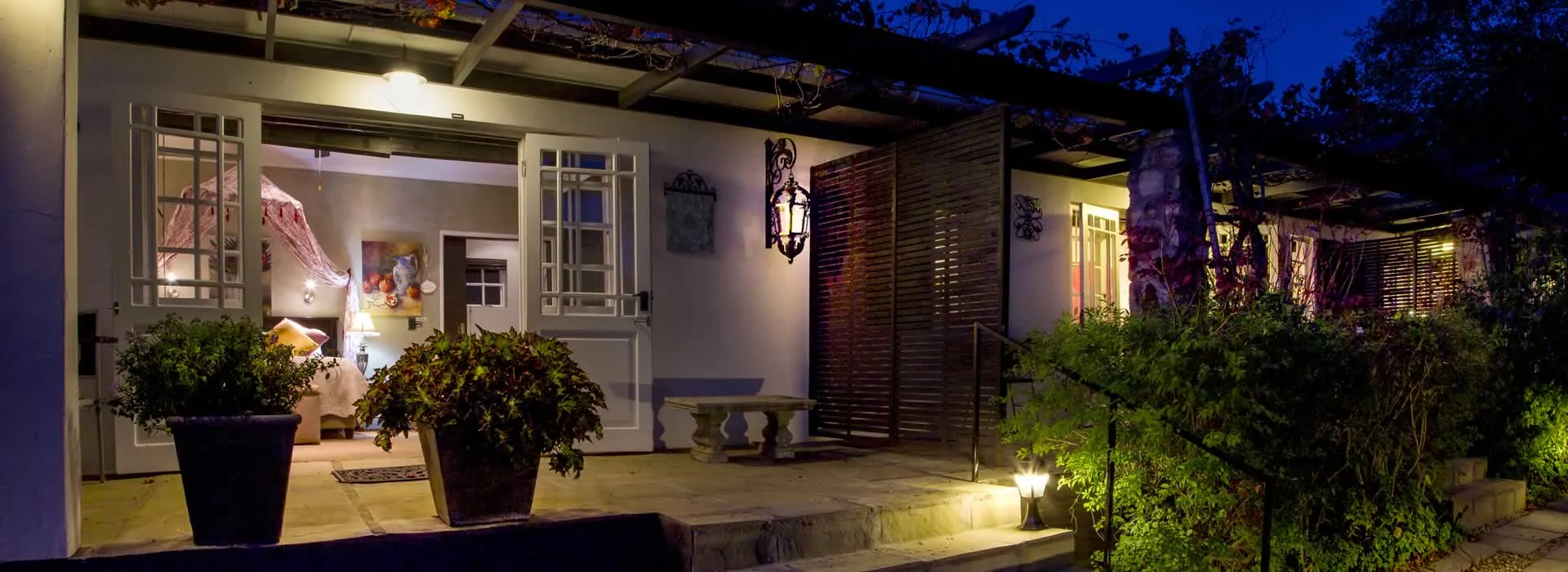 Evening view of a welllit house entrance with potted plants and pathway