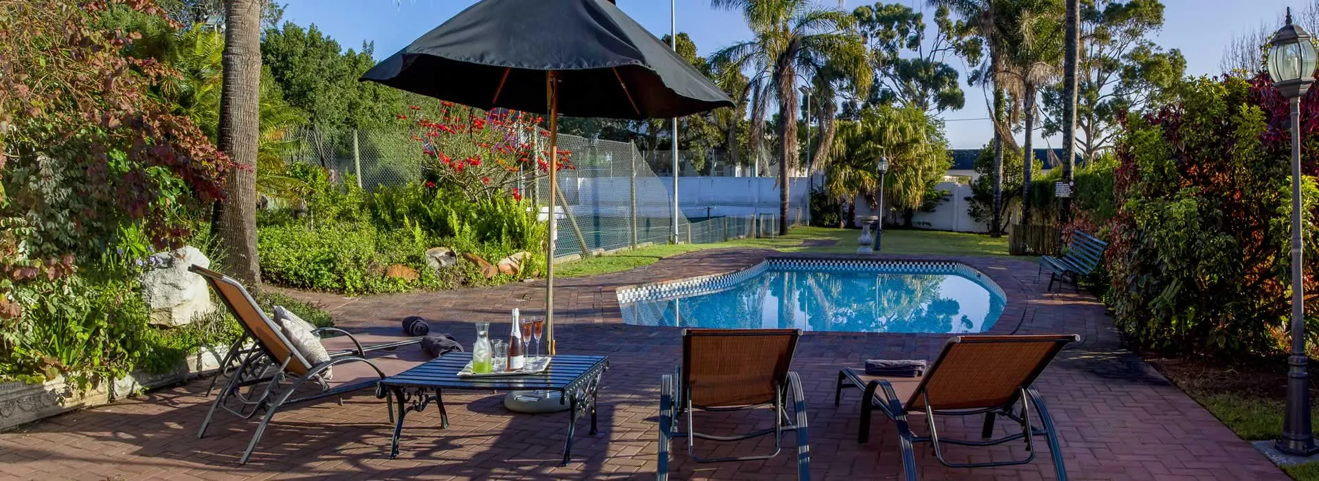 Swimming pool with lounge chairs umbrella and garden in a sunny backyard