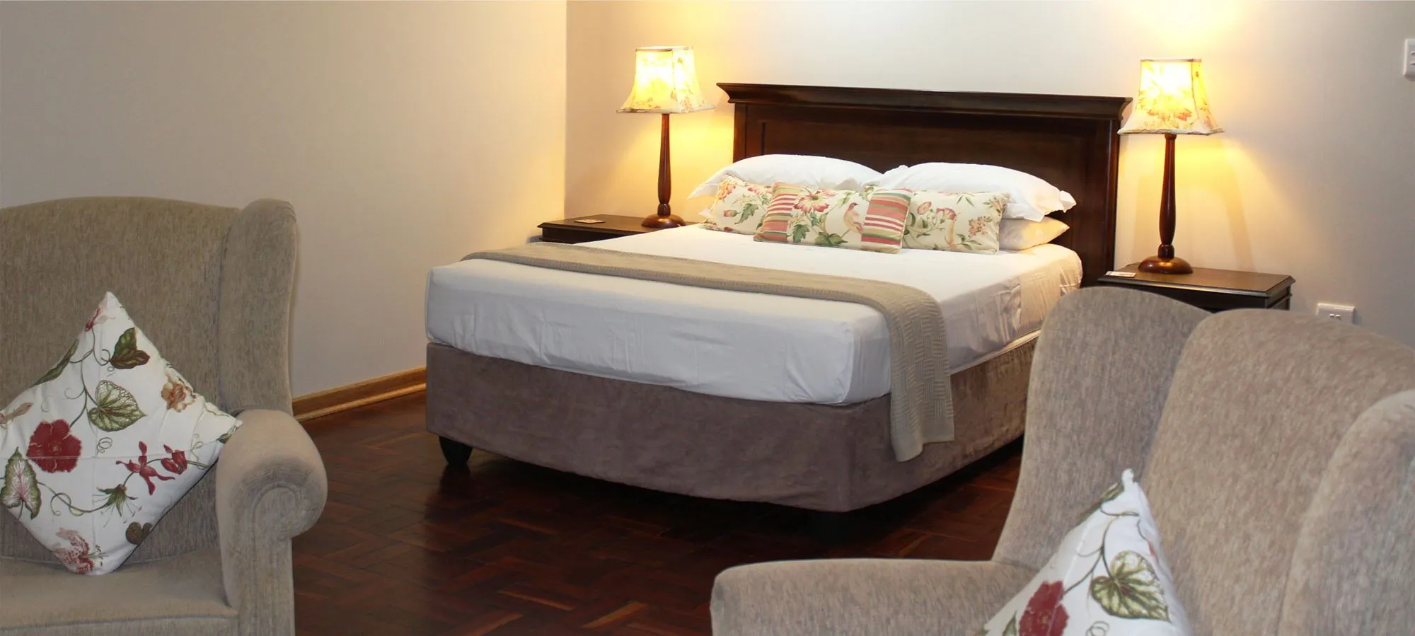 Bedroom with a double bed two armchairs and bedside lamps on wooden floor