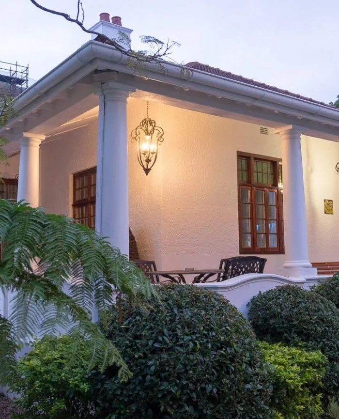 House with a lit lantern on a porch surrounded by greenery