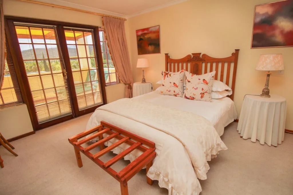 Cozy bedroom with large bed wooden furniture and large windows with curtains