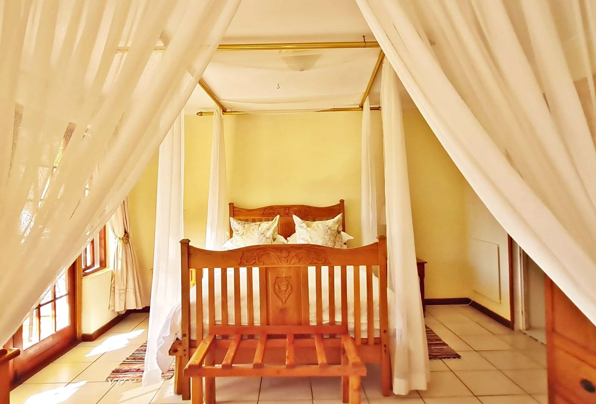 Wooden fourposter bed with white drapes in a bright yellowwalled bedroom
