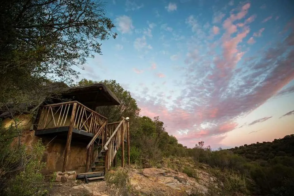 Wooden cabin on stilts in a hilly landscape with a colorful sky