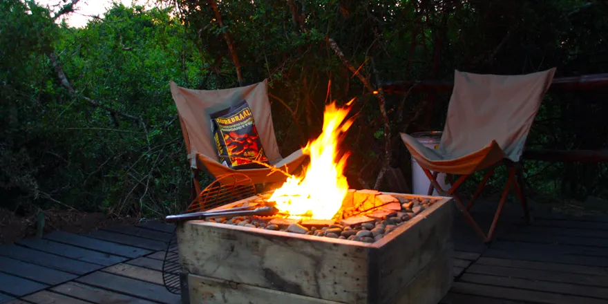 Two chairs around a wooden fire pit with a blazing fire at night