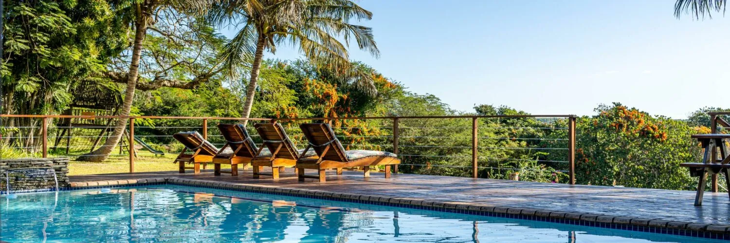 Wooden lounge chairs by a pool with a scenic view of trees and hills