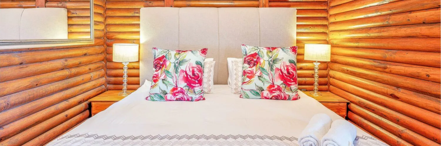 Wooden cabin bedroom with a bed floral pillows and bedside lamps