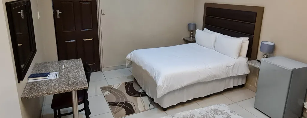 Neat bedroom with double bed desk chair and small refrigerator