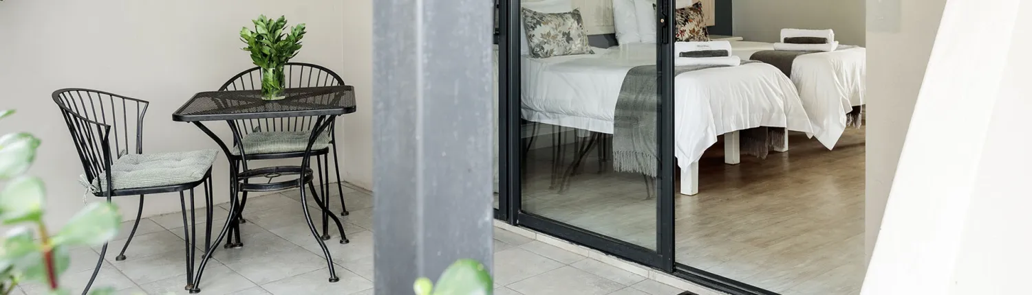 Outdoor seating area with table and chairs next to a bedroom with two beds