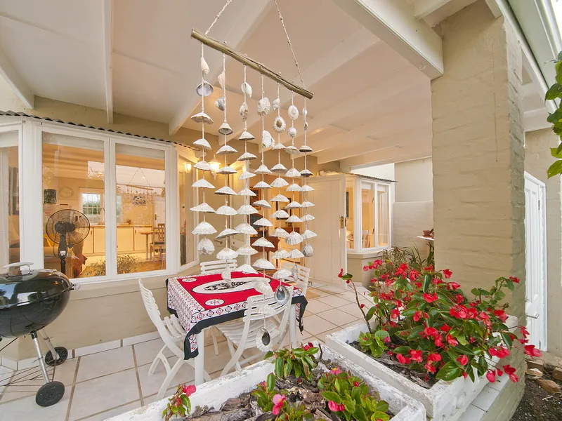 Patio with table chairs and hanging shell decorations surrounded by potted flowers
