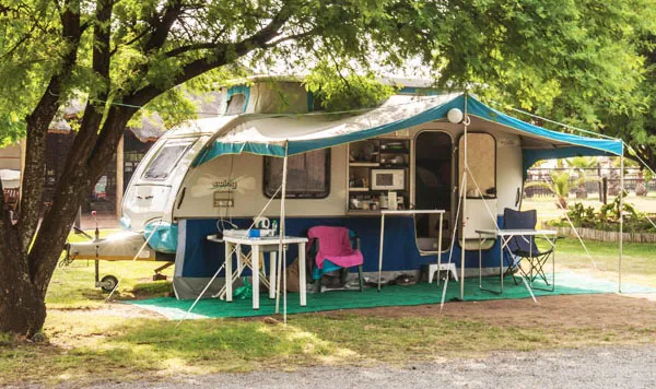 A camper trailer with an awning set up in a shaded campsite
