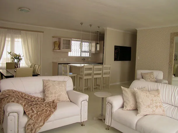 Living room with white sofas patterned cushions and an open kitchen view