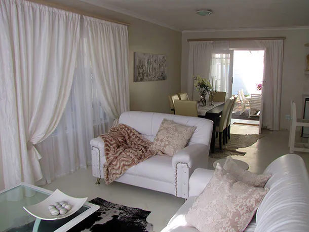 Bright living room with white furniture throw pillows and dining area in background
