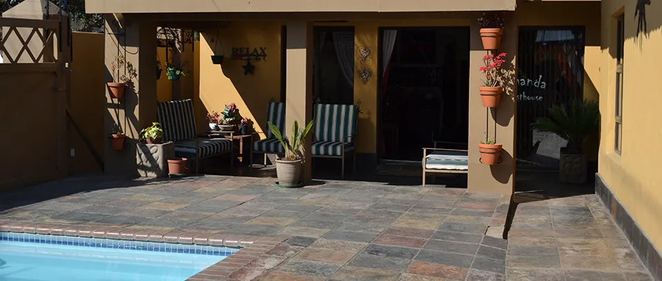 Patio with chairs potted plants and a swimming pool in a sunny courtyard