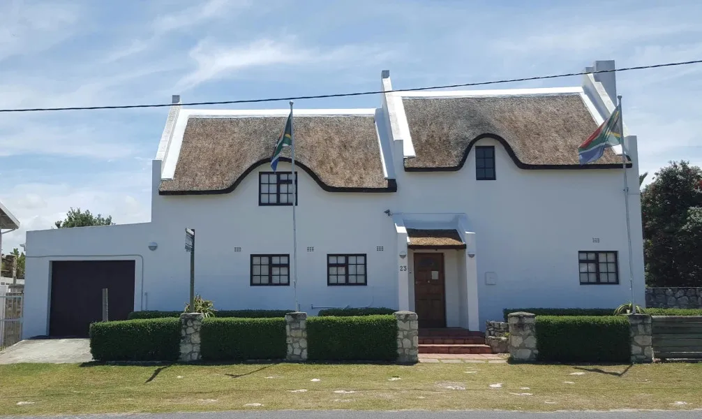 White house with a thatched roof and South African flag in the garden