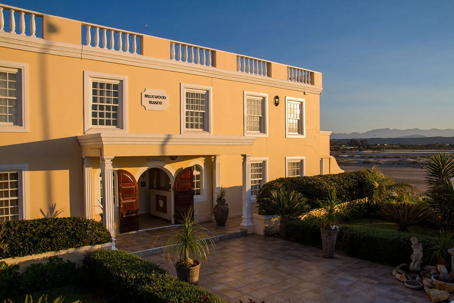 Yellow building with entrance potted plants and garden area at sunset