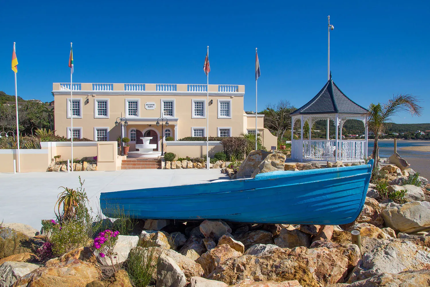 Blue boat on rocks in front of a yellow building with flags