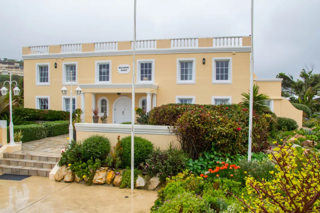 Yellow building with white trim surrounded by lush garden and stone pathway