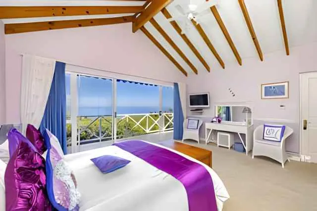 Bedroom with large windows ocean view purple and white decor and wooden ceiling