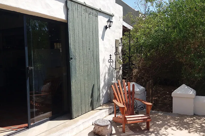 Wooden chair on patio near green door and white building with plants