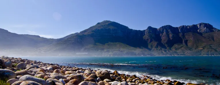 Rocky shoreline with mountains in the background under a clear blue sky