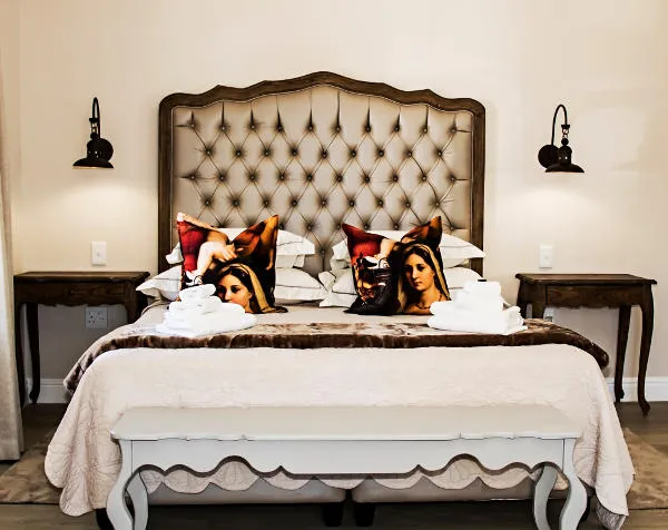 Ornate bed with pillows featuring artwork flanked by wooden bedside tables and lamps