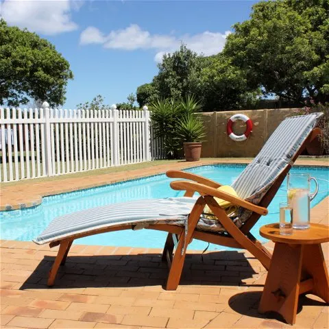 Wooden lounge chair by a pool with a drink on a side table