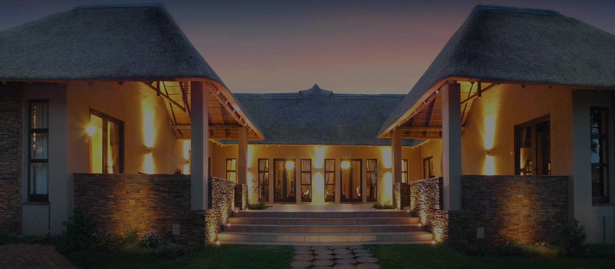 Modern house with thatched roofs, illuminated at dusk.