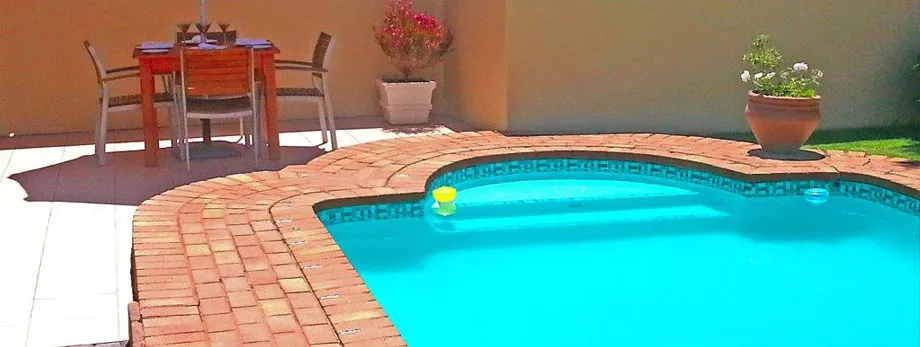 Swimming pool with brick edge outdoor table chairs and potted plants