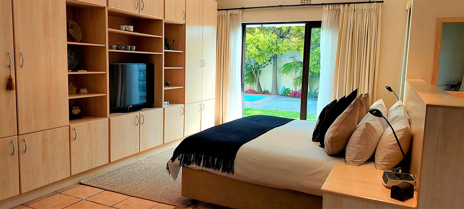 Bedroom with a large bed TV and view of a garden through glass doors