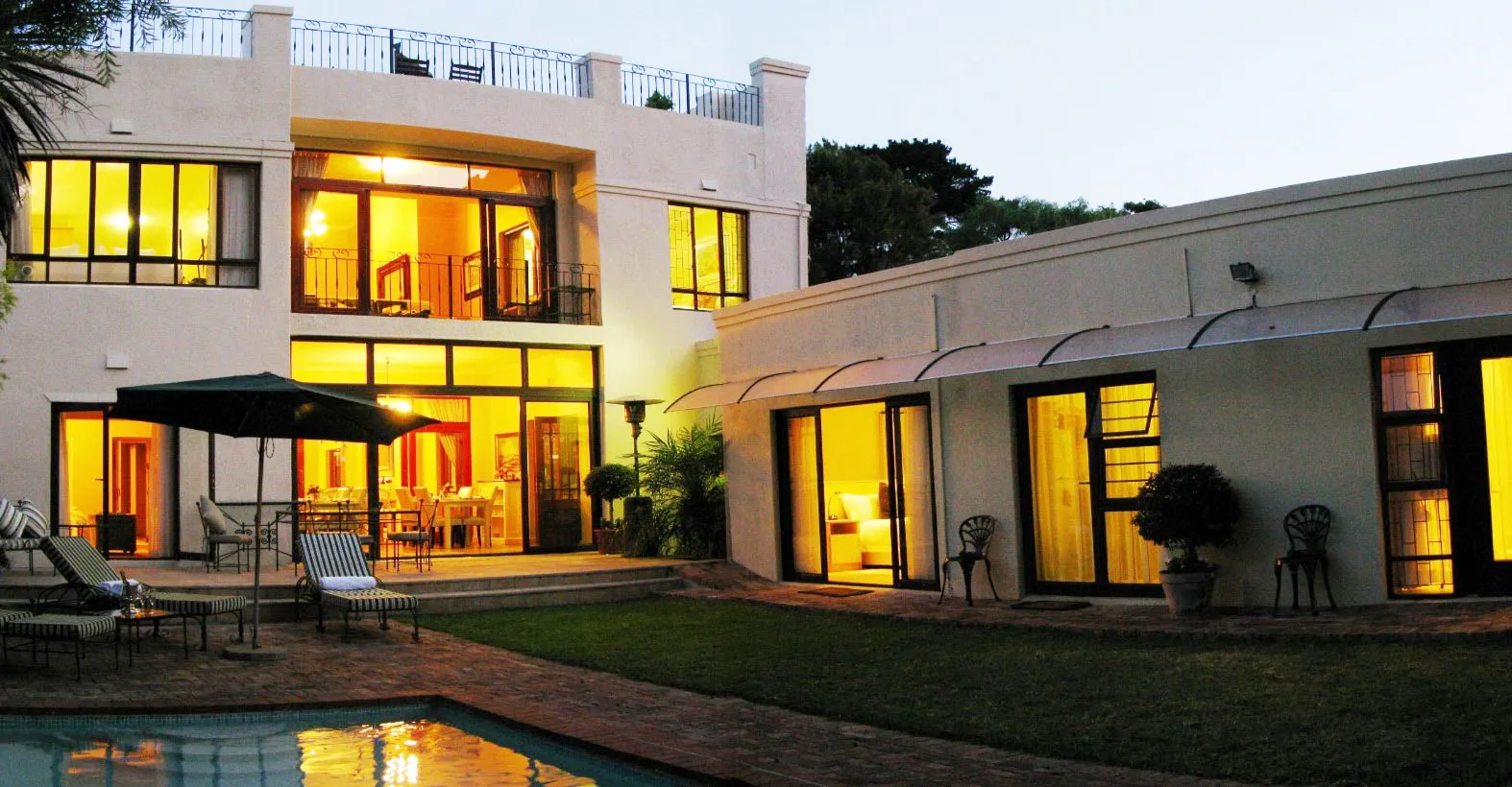 Modern house at night with lit windows pool and garden furniture