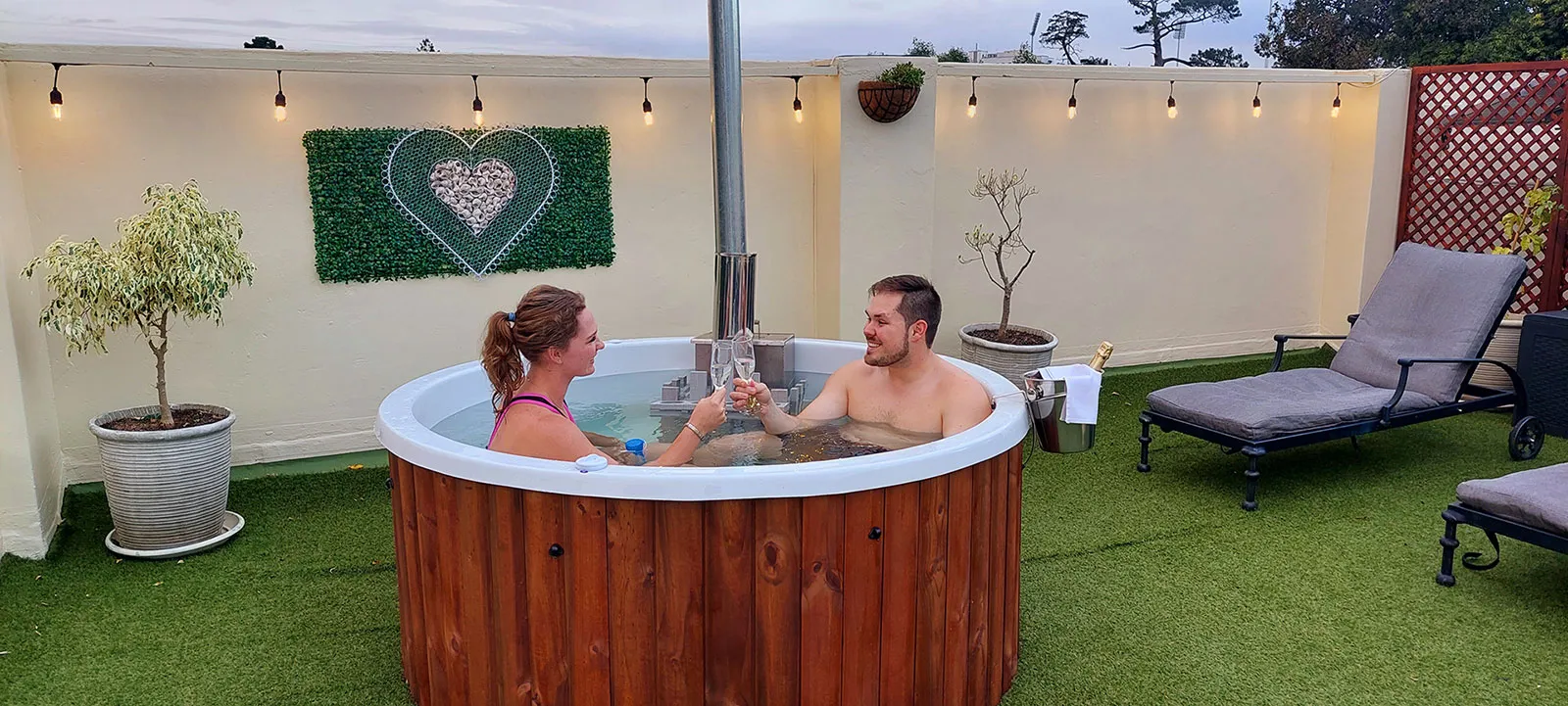 Couple in hot tub toasting with drinks in a decorated outdoor setting