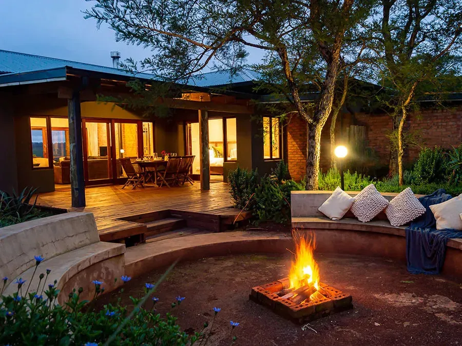 Evening scene with campfire seating area and lit house in background