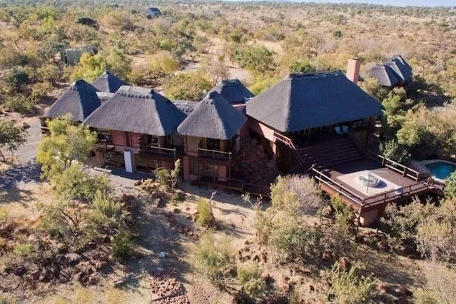 Large lodge with thatched roofs in a dry natural landscape with a pool