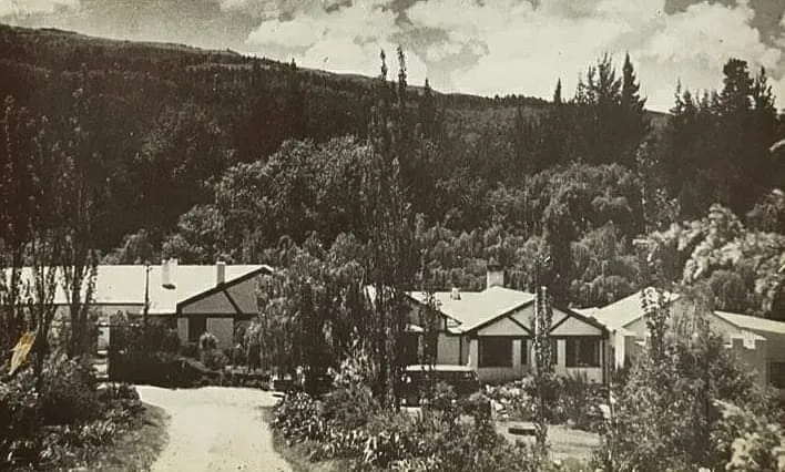 Vintage photo of houses surrounded by trees and hills in the background