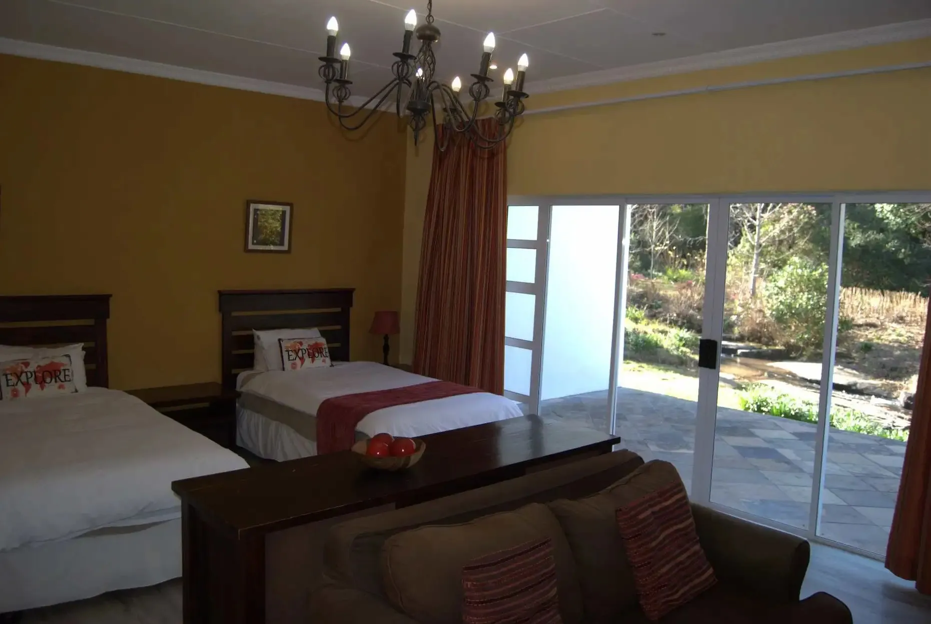 Bedroom with two beds sofa and sliding doors opening to a garden view