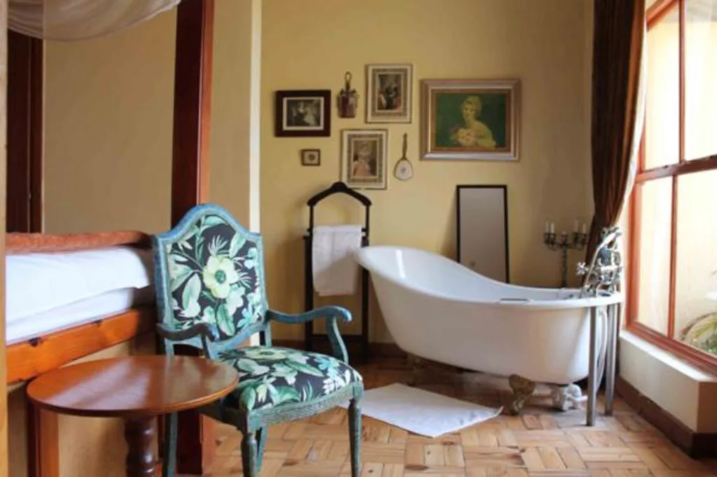 Vintage bathroom with clawfoot tub floral chair and framed pictures on yellow walls