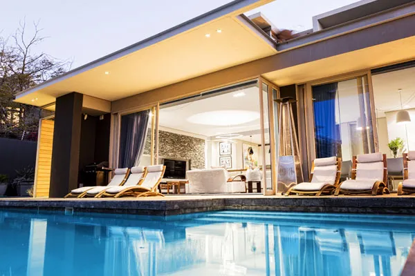 Modern house with pool lounge chairs and open sliding doors at dusk
