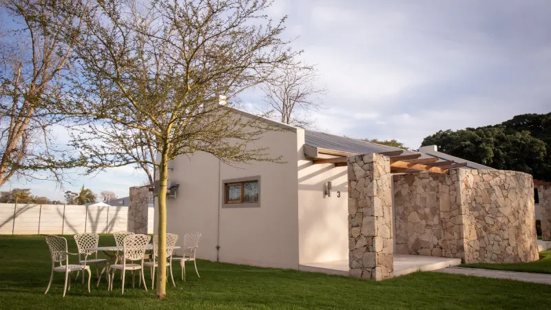 Small stone and stucco house with outdoor seating area and tree in garden