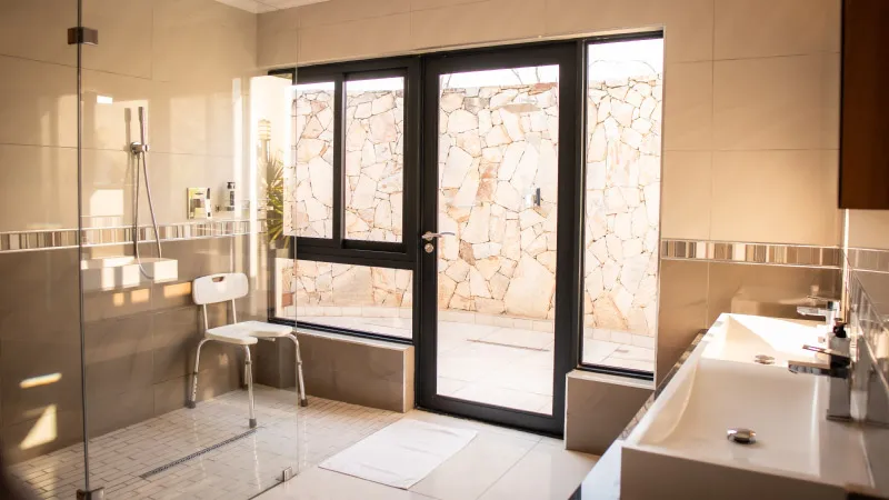Modern bathroom with shower chair sink and large window to stone wall