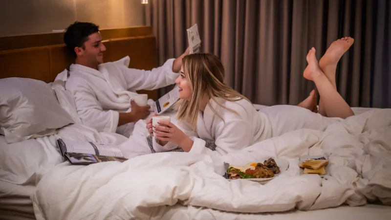 Couple in bathrobes eating breakfast in bed smiling and relaxed