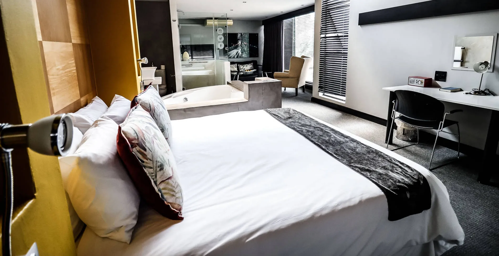 Modern hotel room with large bed desk and bathtub in background