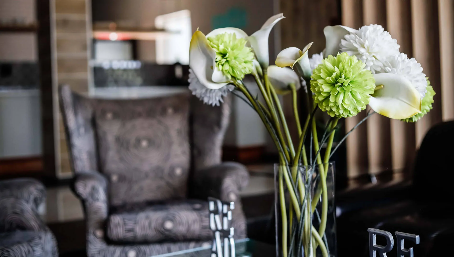 Vase of white and green flowers on a table with an armchair in the background