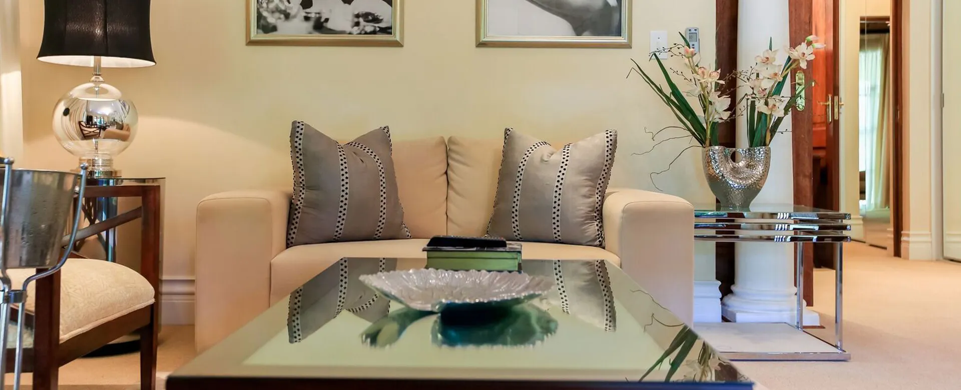 Beige sofa with pillows glass coffee table and floral arrangement in a living room